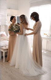 Happy bride with bouquet and bridesmaids in room at home. Wedding day
