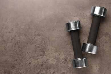 Photo of Metal dumbbells on brown textured table, flat lay. Space for text