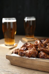 Photo of Tasty chicken wings and glasses of beer on wooden table. Delicious snack
