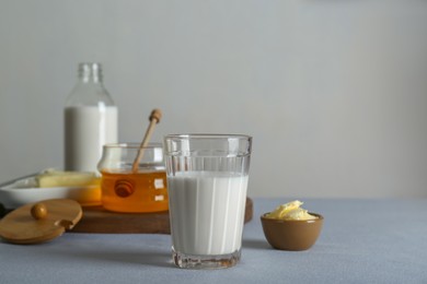 Glass with milk, honey and butter on grey table, space for text