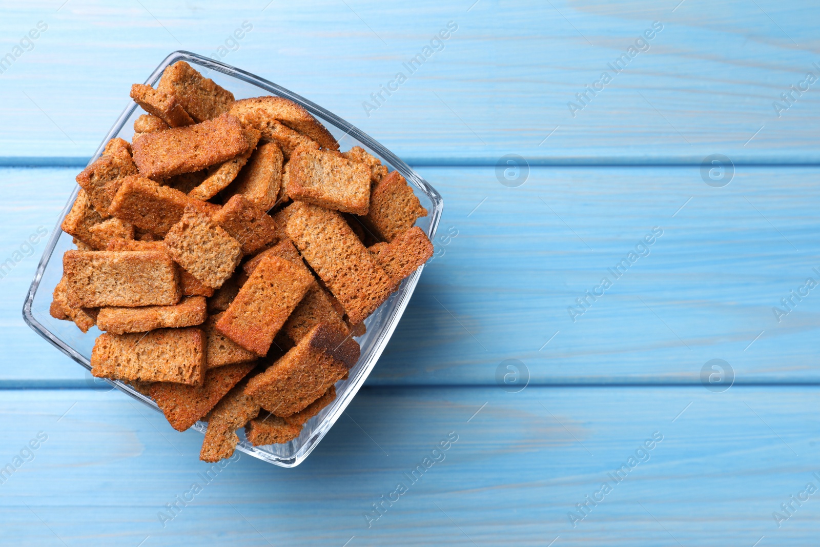 Photo of Crispy rye rusks in bowl on light blue wooden table, top view. Space for text