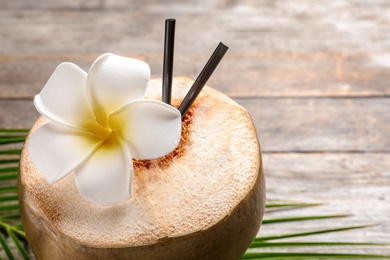 Photo of Fresh green coconut with drinking straws and beautiful flower on table, closeup