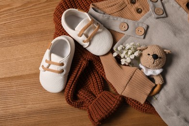 Photo of Children's shoes, clothes and toy on wooden table, closeup