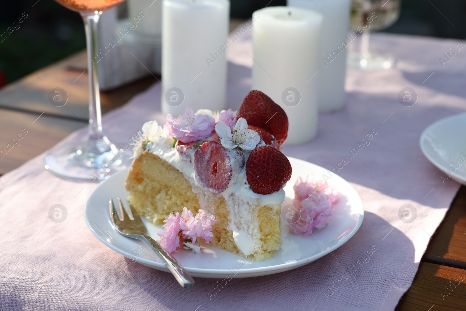 Photo of Piece of delicious homemade cake decorated with fresh strawberries and spring flowers on table outdoors