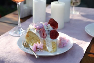 Piece of delicious homemade cake decorated with fresh strawberries and spring flowers on table outdoors