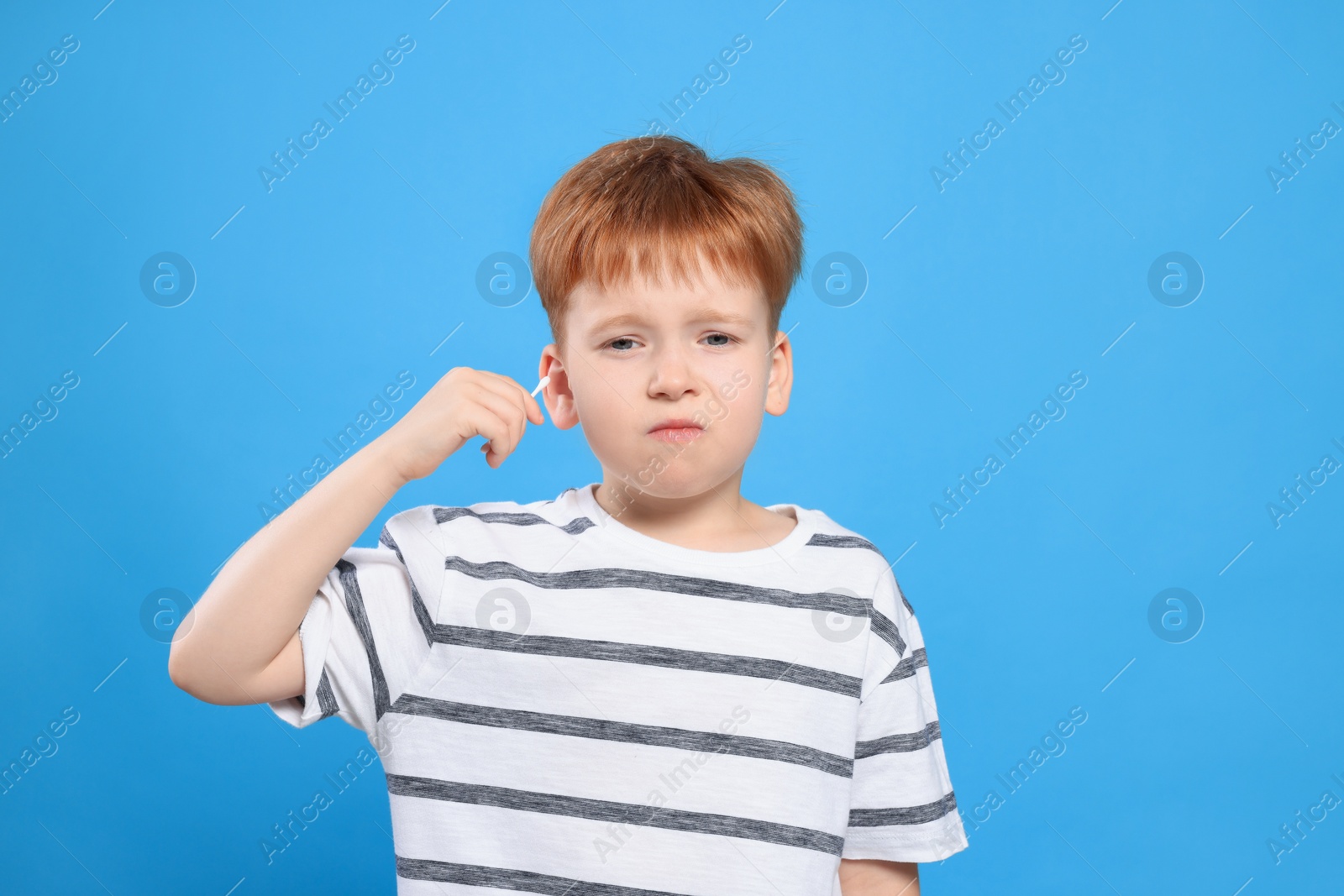 Photo of Little boy cleaning ear with cotton swab on light blue background