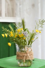 Bouquet of beautiful wildflowers in glass vase on green wooden table outdoors