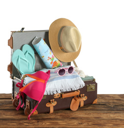 Photo of Open vintage suitcase with different beach objects packed for summer vacation on wooden table against white background