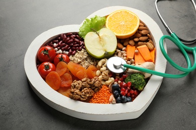 Heart shaped tray with healthy products and stethoscope on grey background
