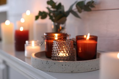 Photo of Burning candles on mantel near white wall indoors