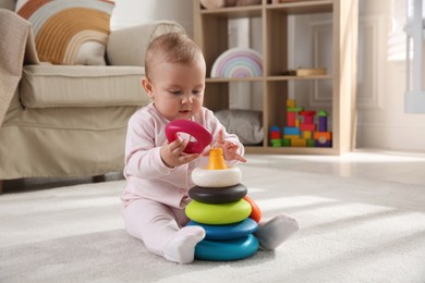 Cute baby girl playing with toy pyramid on floor at home