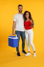 Happy couple with cool box and bottle of beer on yellow background