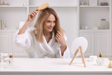 Beautiful woman brushing her hair at vanity in room