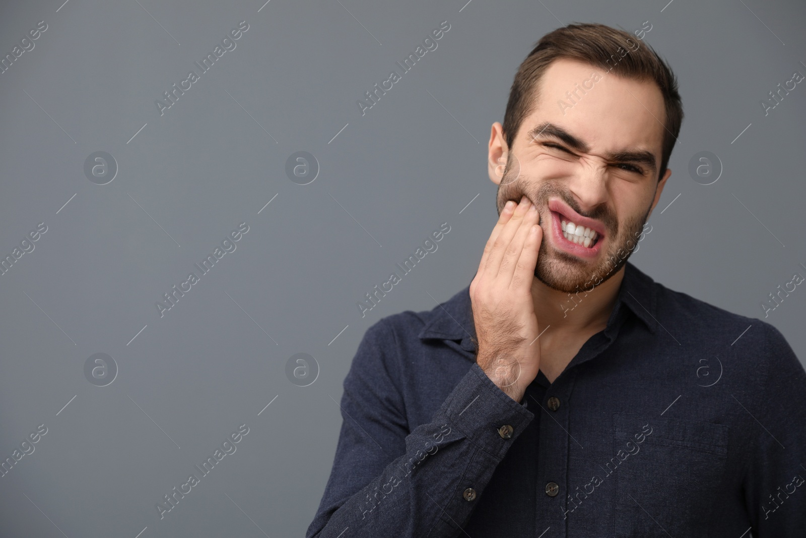 Photo of Young man suffering from strong tooth pain on grey background, space for text