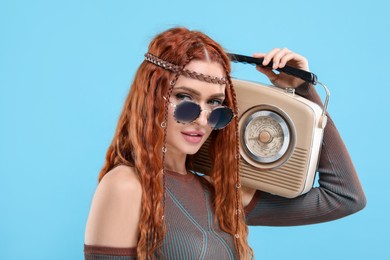 Photo of Stylish young hippie woman with retro radio receiver on light blue background