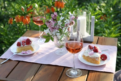 Photo of Vase with spring flowers, wine and cake on table served for romantic date in garden