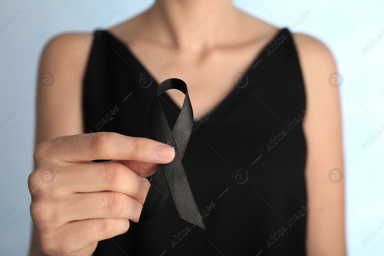 Photo of Woman holding black ribbon on light background, closeup. Funeral symbol