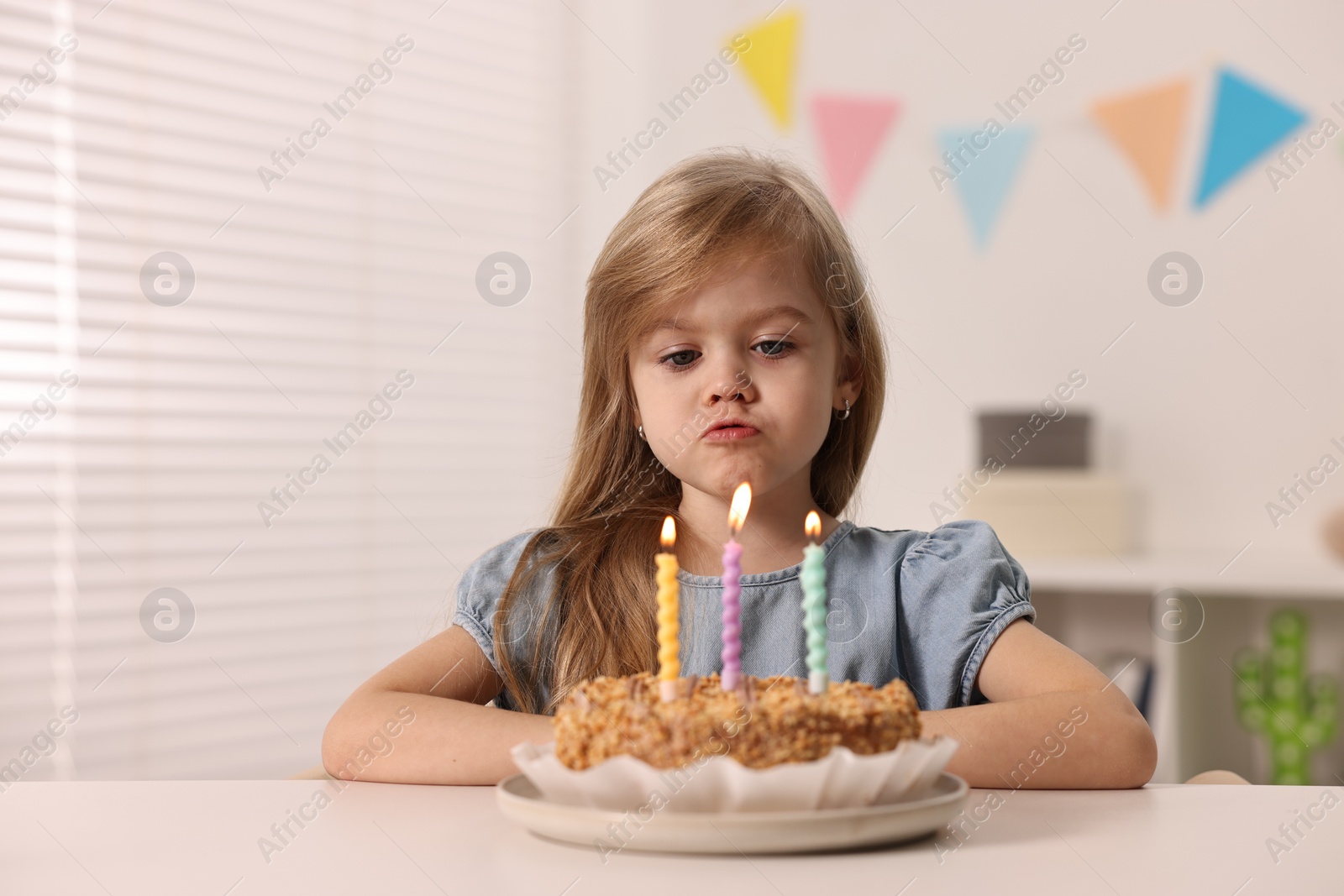 Photo of Cute girl with birthday cake at table indoors