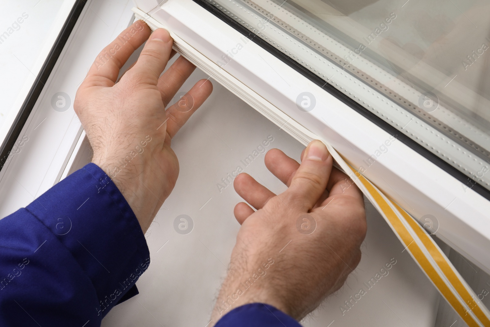 Photo of Worker putting rubber draught strip onto window indoors, closeup