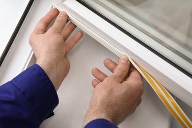 Photo of Worker putting rubber draught strip onto window indoors, closeup