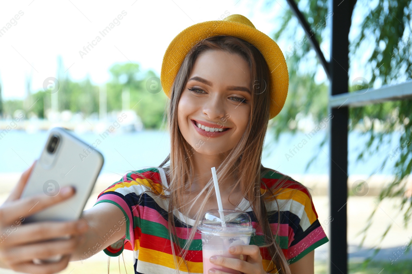 Photo of Happy young woman with drink taking selfie in park