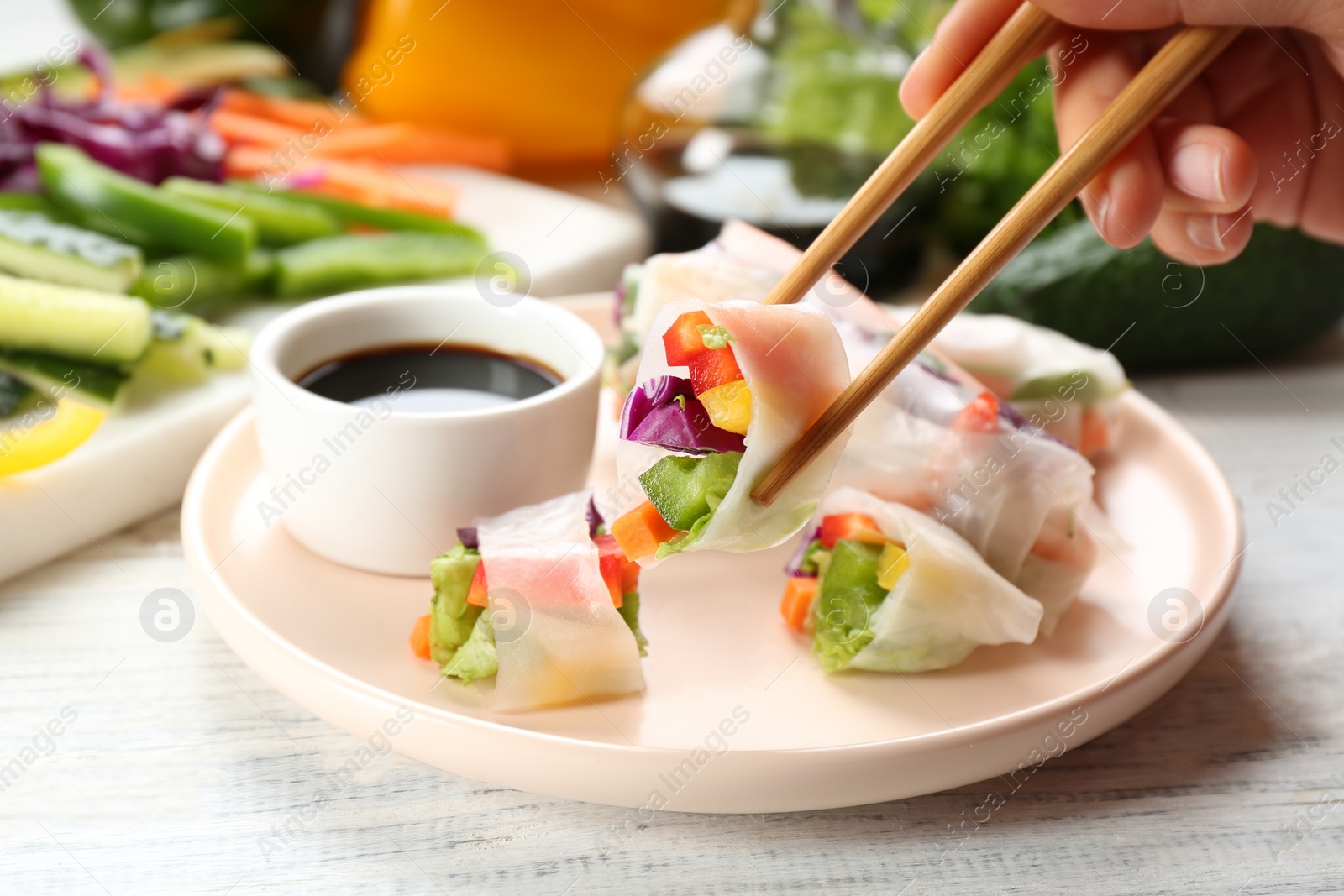 Photo of Woman eating delicious roll wrapped in rice paper at white wooden table, closeup