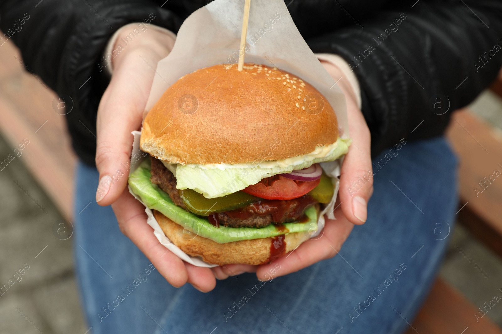 Photo of Woman holding fresh delicious burger outdoors, closeup. Street food