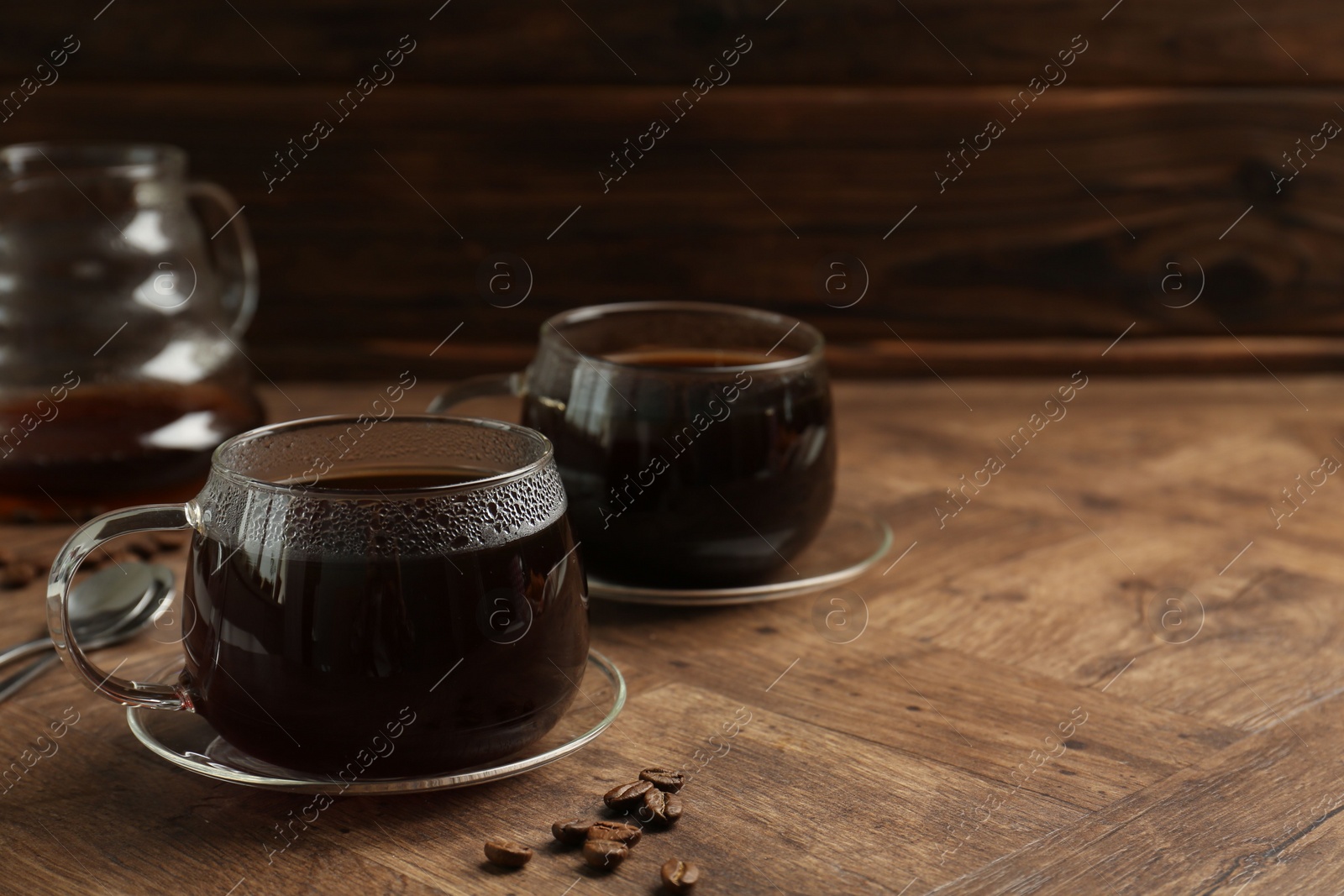 Photo of Hot coffee in glass cups and beans on wooden table, closeup. Space for text