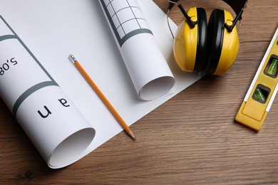 Photo of Construction drawings, safety headphones, pencil and bubble level on wooden table