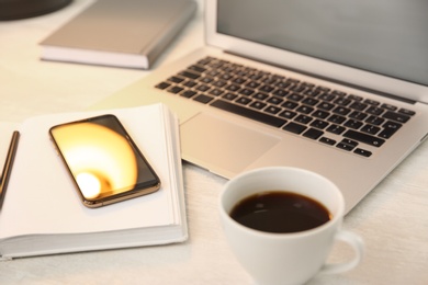 Modern laptop, smartphone, cup of coffee and notebook on white table, closeup