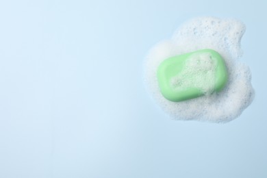 Photo of Soap and fluffy foam on light blue background, top view. Space for text