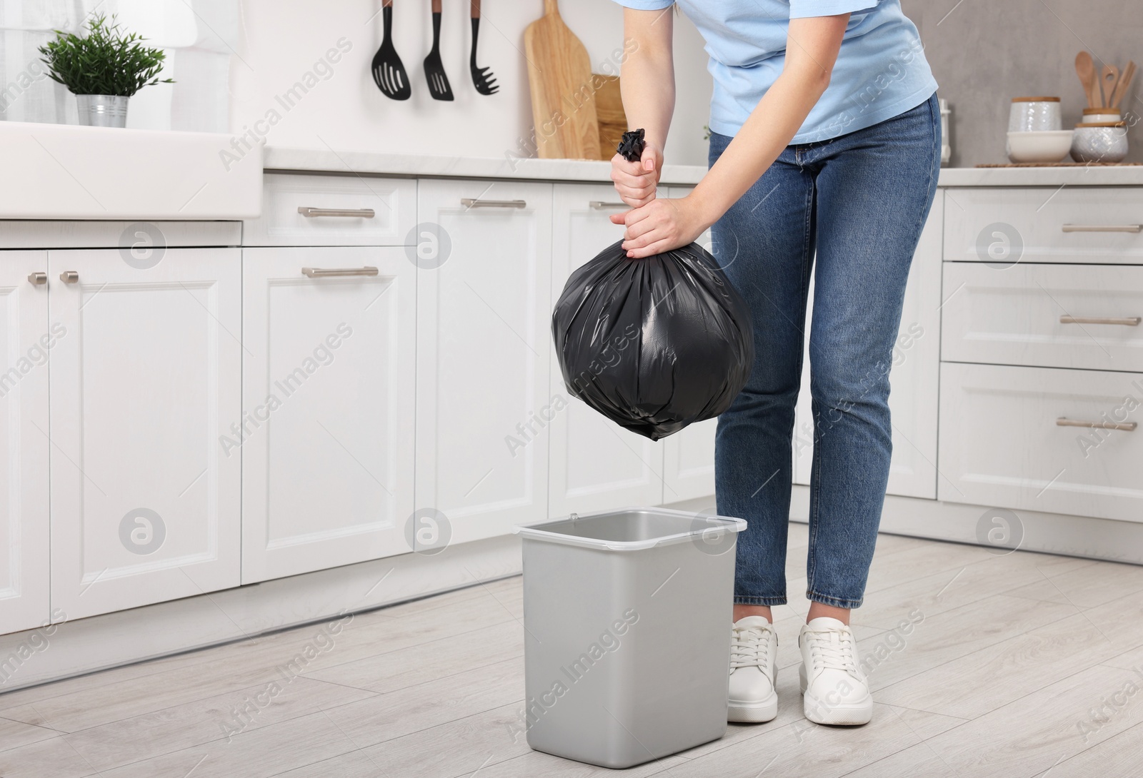 Photo of Woman taking garbage bag out of trash bin in kitchen, closeup