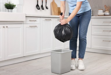 Photo of Woman taking garbage bag out of trash bin in kitchen, closeup