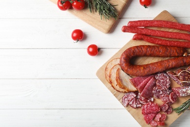 Cutting board with different sliced meat products on wooden background, flat lay. Space for text