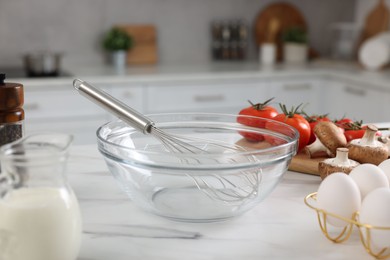 Whisk, bowl, and different ingredients on white marble table indoors