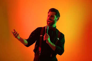 Emotional man with microphone singing in neon lights on orange background