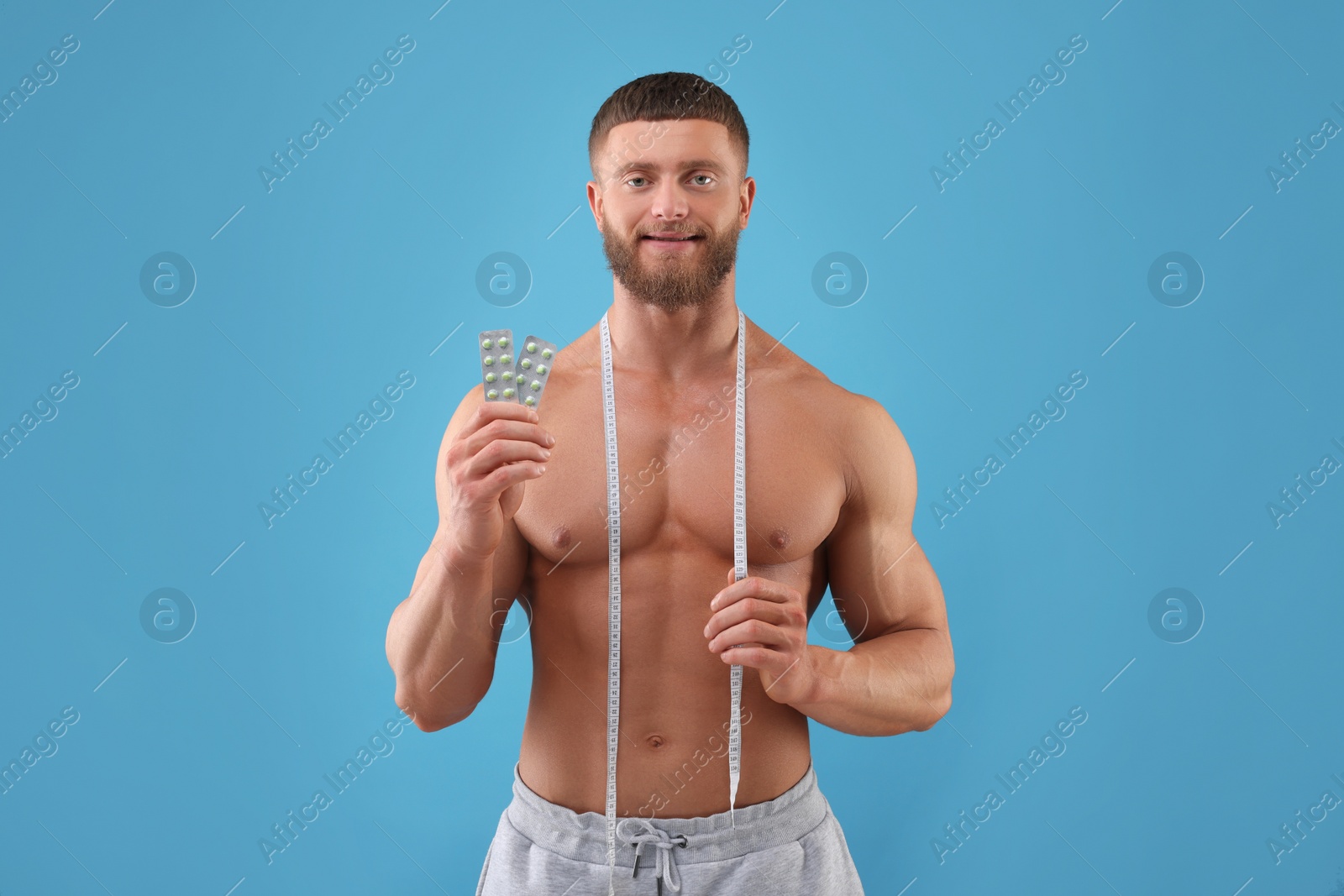 Photo of Athletic young man with measuring tape and pills on light blue background. Weight loss