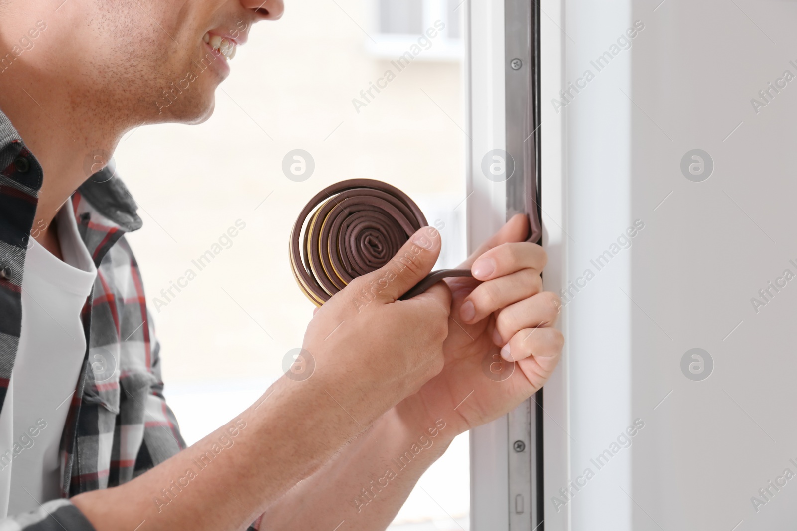 Photo of Young man putting sealing foam tape on window indoors