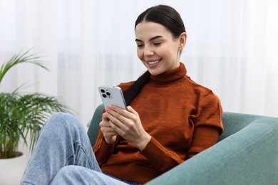 Happy young woman using smartphone on sofa at home
