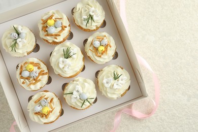 Tasty Easter cupcakes with vanilla cream in box and pink ribbon on beige table, flat lay. Space for text