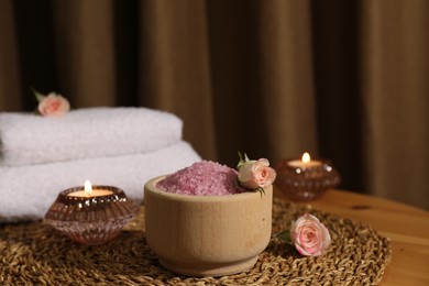 Photo of Bowl of pink sea salt, roses, burning candles and towels on wooden table