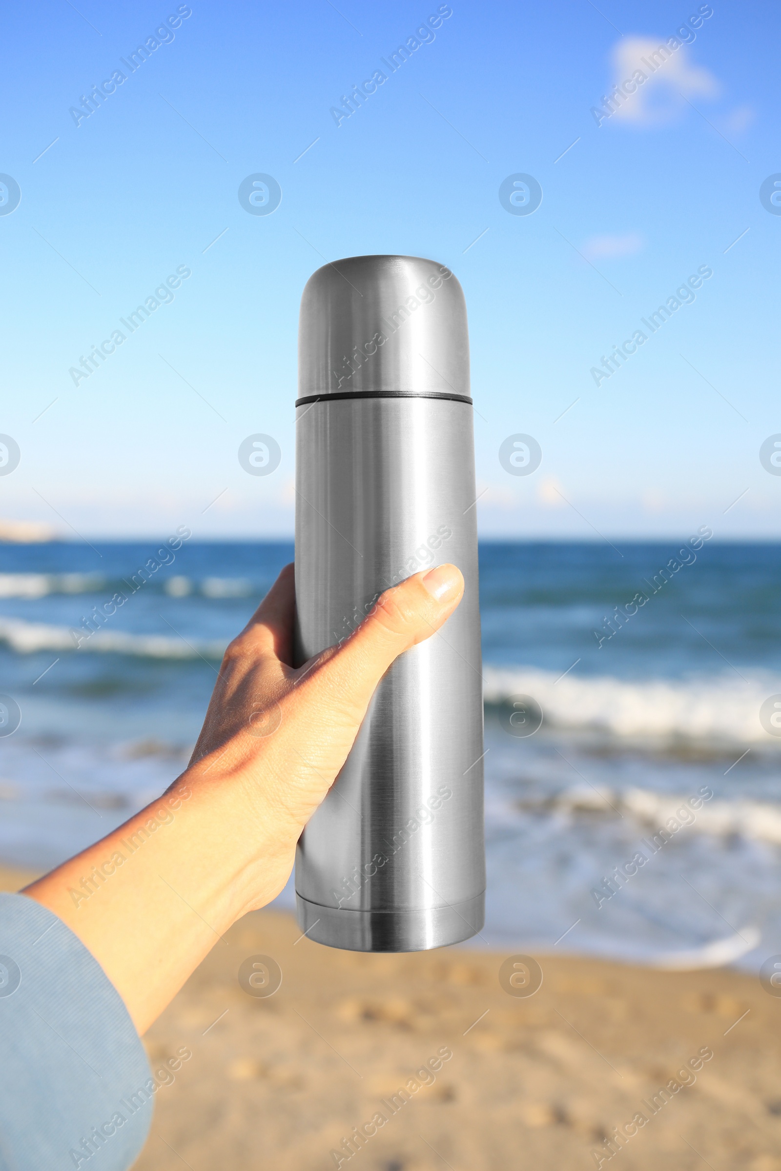 Photo of Woman holding metallic thermos with hot drink on beach near sea, closeup