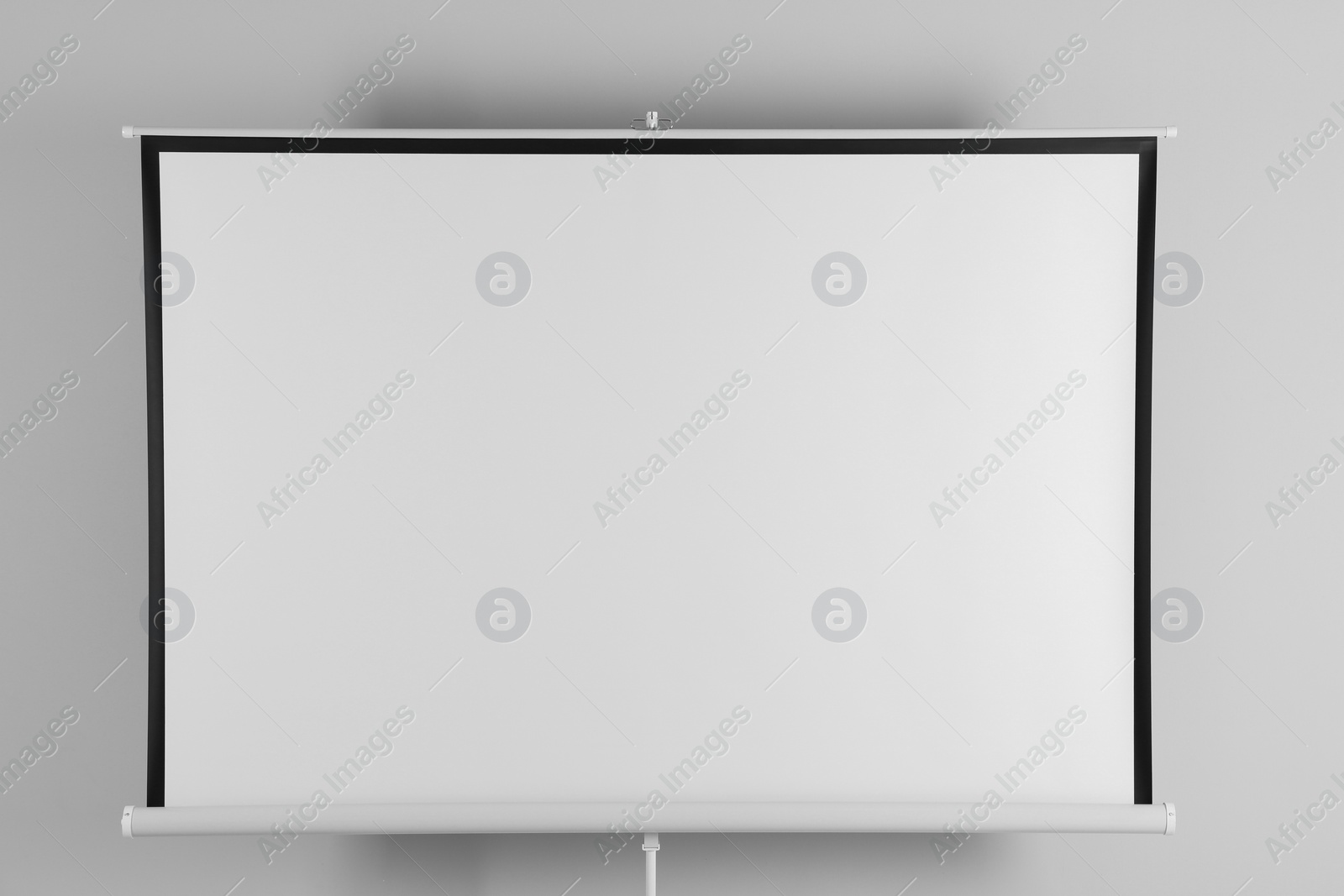 Photo of Blank projection screen near white wall indoors. Space for design