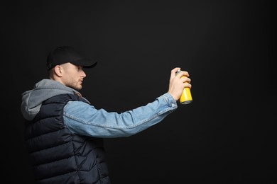 Handsome man holding used can of spray paint on black background