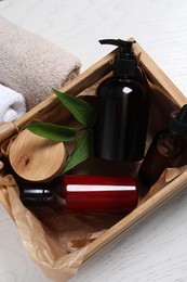 Photo of Crate with different cosmetic products, towels and leaves on white wooden table, flat lay