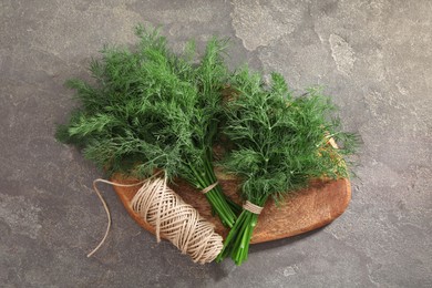 Bunches of fresh dill and spool of thread on grey textured table, top view