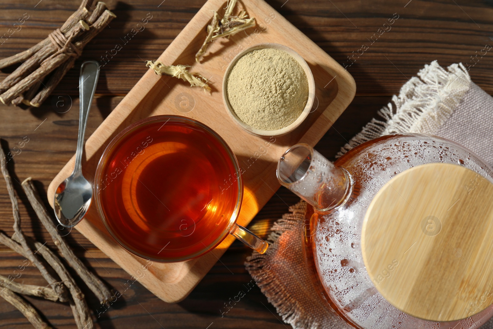 Photo of Aromatic licorice tea in cup, dried sticks of licorice root and powder on wooden table, flat lay