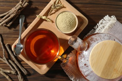 Aromatic licorice tea in cup, dried sticks of licorice root and powder on wooden table, flat lay