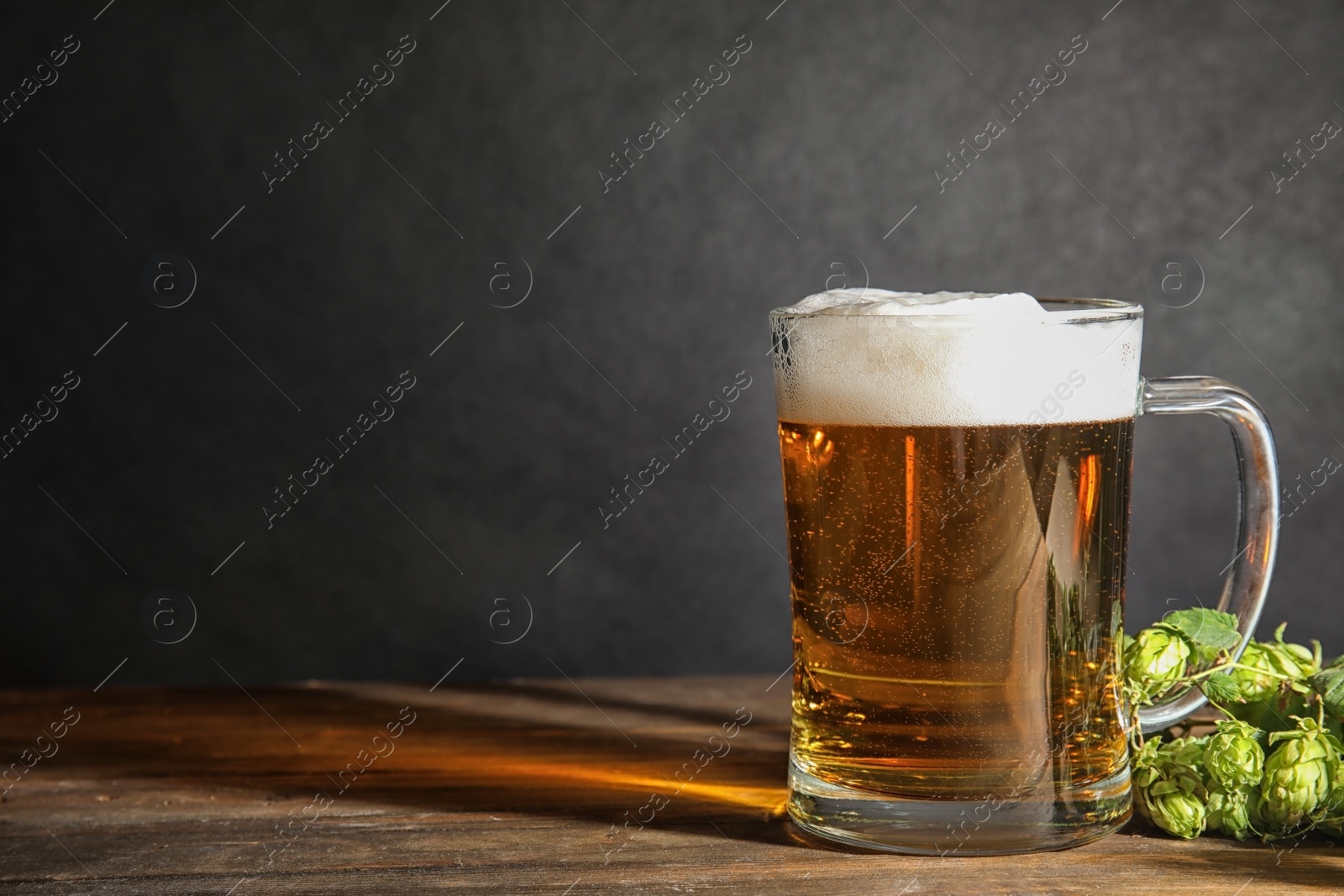 Photo of Composition with tasty beer and fresh green hops on wooden table. Space for text