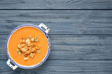 Photo of Tasty creamy pumpkin soup with croutons and seeds in bowl on blue wooden table, top view. Space for text